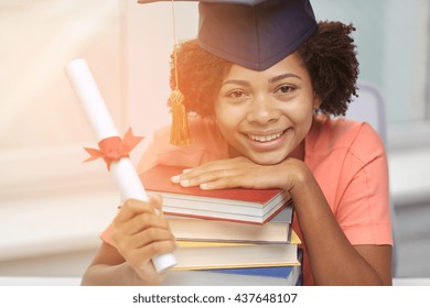 Education, School, Graduation And People Concept - Happy Smiling African American Student Girl In Bachelor Cap With Books And Diploma Sitting At Table At Home