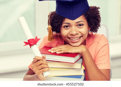 Education, School, Graduation And People Concept - Happy Smiling African American Student Girl In Bachelor Cap With Books And Diploma Sitting At Table At Home