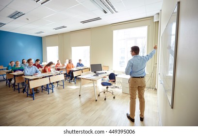 education, school, learning, teaching and people concept - teacher standing in front of students and showing something on white board in classroom