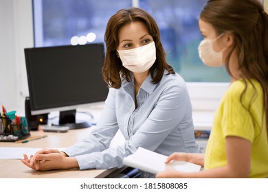 education, school and pandemic concept - teacher and little student girl wearing face protective medical masks for protection from virus disease in classroom - Powered by Shutterstock