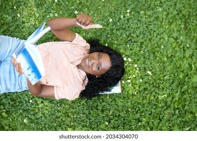 Education, School And People Concept - Happy Smiling African American Student Girl Reading Math Textbook Lying On Grass And Showing Thumbs Up