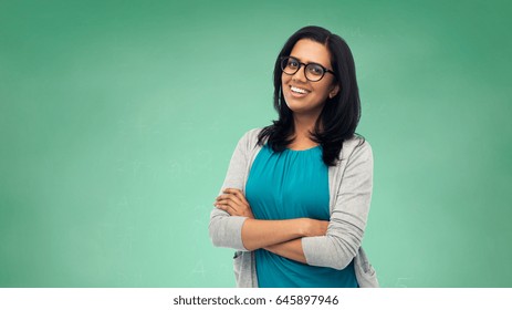 Education, School And People Concept - Happy Smiling Young Indian Student Woman Or Teacher In Glasses Over Green Chalkboard Background