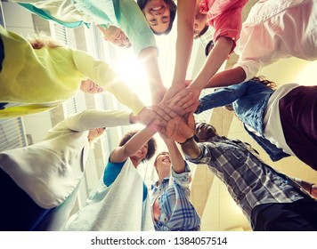 Education, School, Teamwork And People Concept - Group Of International Students With Hands On Top Of Each Other Over Table