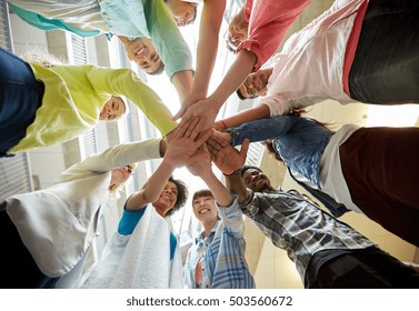 Education, School, Teamwork And People Concept - Group Of International Students With Hands On Top Of Each Other Over Table