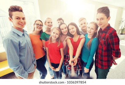 Education, School, Technology And People Concept - Group Of Happy Smiling Students Taking Picture With Smartphone Selfie Stick In Corridor