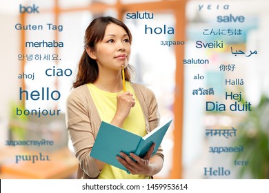 education, school and translation concept - asian student or creative woman with diary and pencil thinking over greeting words in different foreign languages