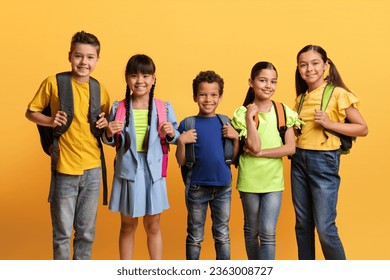 Education, Schooling Concept. Group of diverse multiracial schoolchildren happy boys and girls smiling at camera, wearing casual outfit and carrying backpack, yellow orange color studio background - Powered by Shutterstock