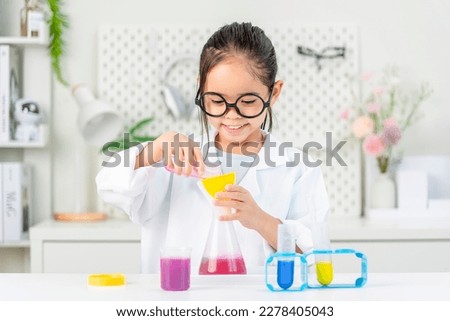 education, science and children concept girl in goggles with magnifier studying test tube with chemical at home laboratory