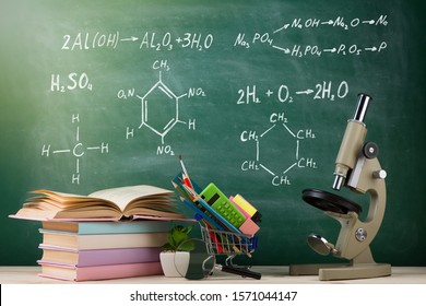 Education And Science Concept - Group Of Colorful Books And Microscope On The Wooden Table In The Classroom, Blackboard Background