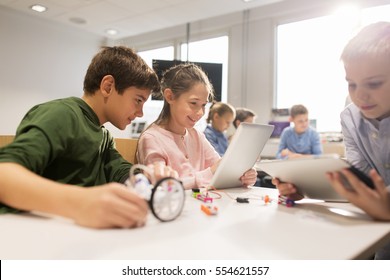 education, science, technology, children and people concept - group of happy kids or students with tablet pc computer programming electric toys and building robots at robotics school lesson - Shutterstock ID 554621557