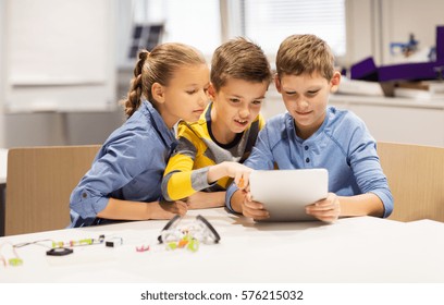 Education, Science, Technology, Children And People Concept - Group Of Happy Kids Or Students With Tablet Pc Computer Programming Electric Toys And Building Robots At Robotics School Lesson