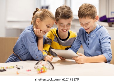 Education, Science, Technology, Children And People Concept - Group Of Happy Kids Or Students With Tablet Pc Computer Programming Electric Toys And Building Robots At Robotics School Lesson