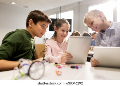 education, science, technology, children and people concept - group of happy kids or students with tablet pc computer programming electric toys and building robots at robotics school lesson
