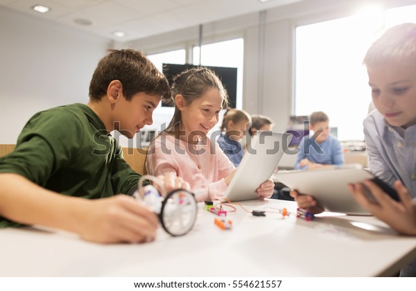 education,\
science, technology, children and people concept - group of happy\
kids or students with tablet pc computer programming electric toys\
and building robots at robotics school\
lesson