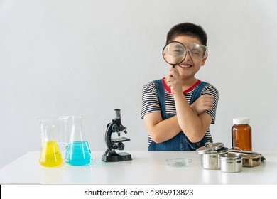 Education scientists concept. Little kid scientific boy holding magnifying in his hand front view eye with microscope and tube experiment on the desk while looking at something at science lab room.  - Powered by Shutterstock