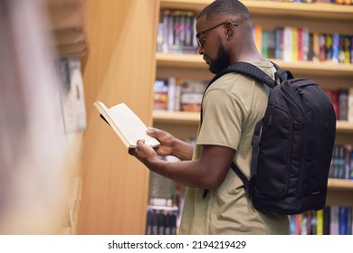 Education Student With Book In A Library At University, College Or School Reading Or Doing Research. Scholarship, Learning And Study Knowledge And Black Man With Print Books On Shelf And Backpack