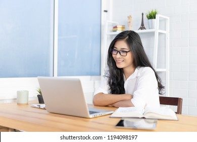Education study abroad,Asian student girl wear glasses table looking book while do homework with laptop making video call abroad using internet friend connection, happy mood smiling broadly in library