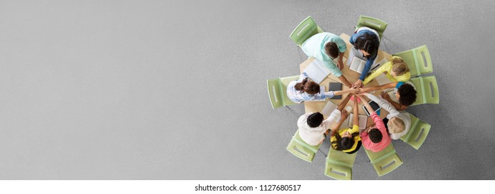 education, teamwork and people concept - group of international students with books and tablet pc computers putting hands on top of each other sitting at round table - Powered by Shutterstock