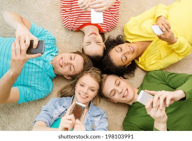 education, technology and happiness concept - group of young smiling people lying down on floor in circle with smartphones - Powered by Shutterstock