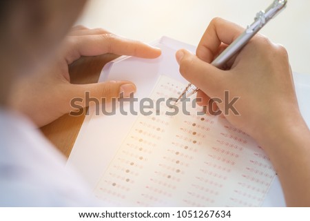 Education test concept : Hands student holding pen for testing exams writing answer sheet or exercise for taking fill in exam carbon paper computer on wood table at classroom in high school.