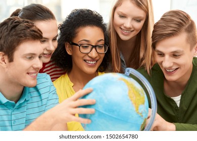 education, travel and geography concept - happy high school students or friends looking at earth globe