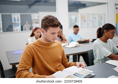 Education, University Student And Man Reading Book In Classroom, Studying Or Assignment Research. Learning, College And Person With Textbook, Exam Or Test Preparation And Knowledge Search At Desk.