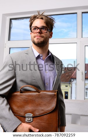 Education and work concept. Serious man or professor, teacher or worker with beard and messy hair in nerd glasses. Man with briefcase on glass door background. Nerd or brainiac wearing classic jacket