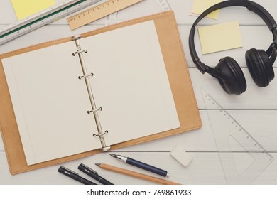 Education and work concept, top view shot of workplace. Stationery supplies - blank notepad and headphones on white wooden desktop, flat lay, copy space, mockup