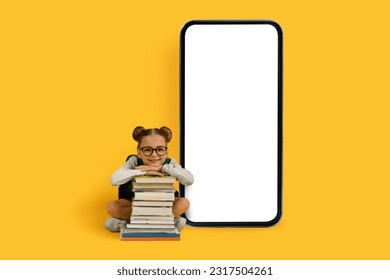 Educational App. Cute Little Girl With Pile Of Books Sitting Near Big Blank Smartphone With White Screen, Smiling Preteen Female Child Recommending Mobile Application For Study, Mockup - Powered by Shutterstock