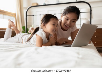 Educational App For Kids, Younger Generation And Modern Technologies For Fun And Development, Parental Control Concept. Asian Mother And Little Daughter Lying In Bed With Laptop Spend Time In Internet