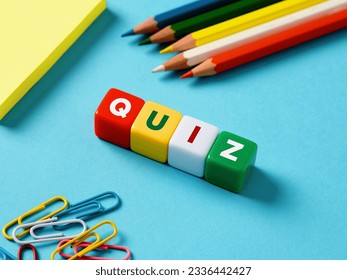 Educational exam or question games concept. The word quiz on colorful cubes wit stationery objects on blue background.