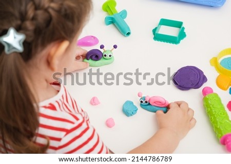 educational games with plasticine, little girl make snails on white table with playing dough, top view