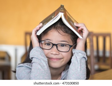 Educational Literacy, World Book Day Concept With Smart Asian School Student Kid With Eyeglasses Having Children Book Over Her Head