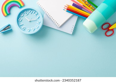 Educational materials concept. Overhead view showcasing notepads, clock and a variety of learning tools against a pastel blue isolated backdrop. Copy-space available for text or promotional material