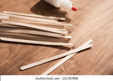 Educative Craft. Popsicle Sticks And Bottle Of White Glue On Wooden Workdesk.