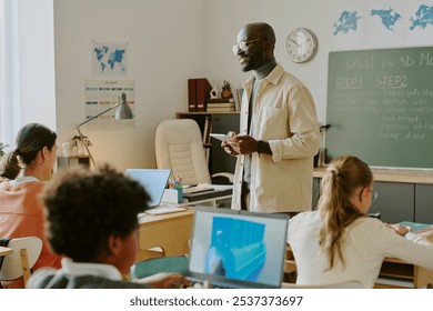 Educator instructing students in classroom on 3D modeling with instructional materials and technology visible. Multiracial group of focused students learning new skills - Powered by Shutterstock