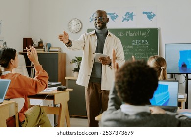 Educator pointing towards students while taking questions in classroom during 3D modeling lesson, fostering interactive learning environment with diverse group