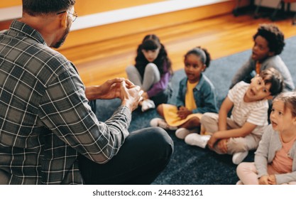 Educator teaches an elementary school class. Man talking in front of a group of children. Male teacher giving a basic verbal lesson, he teaches kids the vowel sounds.