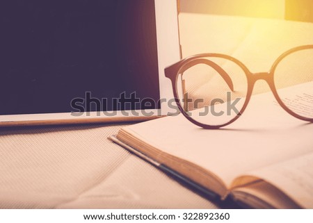 Eduction concept. Open old book with eye glasses and tablet PC background. Vintage filter.