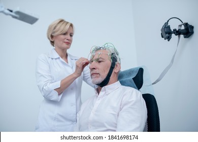 EEG Examination. Female Neurologist Adjusting Electrode Cap On Gray-haired Male Patient Head