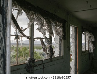 Eerie interior of an abandoned stone cabin along Highway 395, in California. Tattered curtains blow inward as the wind sweeps through the broken windows, 
