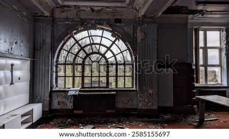 Eerie patterned window arch at abandoned Wheelwright Boys Grammar School in Dewsbury. Derelict college building with broken gothic arched glass windows, peeling wall paint and gloomy haunted looking room. Deteriorating education classroom  crumbling in former stately home.