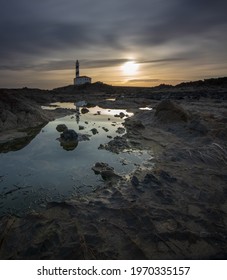 An Eerie Scenery Of A Lighthouse Under The Golden Sky On The Rocky Shore Of The Ocean