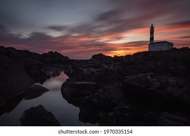 An Eerie Scenery Of A Lighthouse Under The Pink And Golden Sky In The Bay Of The Ocean