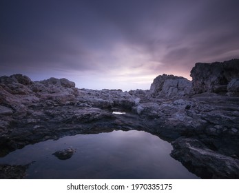 An Eerie Scenery Of Rocky Outcrops In The Ocean Under The Purple Sky