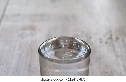 The Effect Of Surface Tension, Pure Water In A Glass Cup Forms A Dome. Neutral Wood Background In Soft Focus.