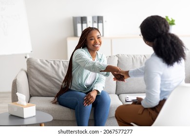 Effective therapy. Cheerful female patient and psychologist shaking hands at office. African American woman feeling grateful to her psychotherapist after successful treatment