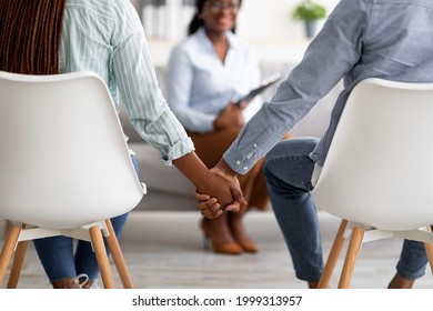 Effective therapy concept. Back view of unrecognizable black couple holding hands and female psychologist on background in office. Family reconciling after successful psychotherapy, closeup
