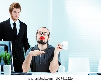 An effeminate male office worker wearing bright red lipstick sitting at his desk simpering watched in disgust by a colleague in a smart suit and tie - Shutterstock ID 1019811226