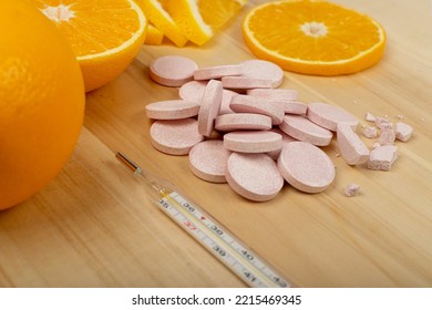 Effervescent Orange Tablets With Medical Thermometer. Fizzy Fruit Tablets Pile, Disease Prevention Concept, Pink Orange Effervescent Vitamine Supplement On Wood Background